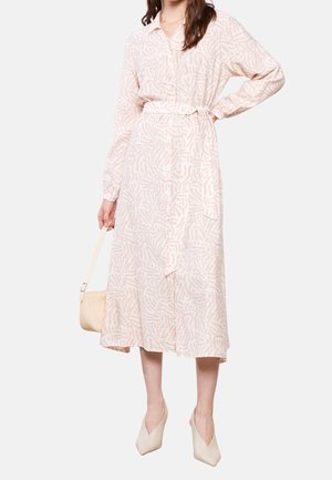 Woman wearing a light pink patterned long-sleeve midi dress with buttons and a waist tie, holding a beige handbag and wearing beige heels.