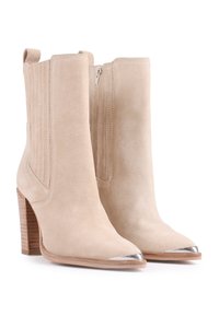 Botas de tobillo de ante beige con puntera puntiaguda, detalles metálicos plateados, paneles laterales acanalados y un tacón de madera apilada. Incluyen una cremallera lateral.