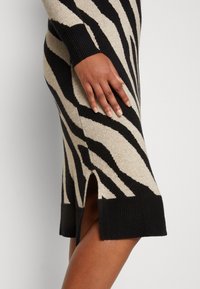 Stickad klänning med ett zebramönster i svart och beige, med ribbad fåll och slits på sidan för ökad stil och komfort.