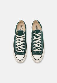 Zelené plátěné tenisky s bílými tkaničkami, gumovým příívodem na špičce, krémovou podešví a zdobným prošíváním. Navrženy v klasickém stylu nízkých tenisek.