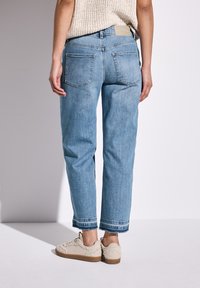 Vaqueros de denim de color azul claro con un corte relajado, que presentan dobladillos deshilachados, dos bolsillos traseros y una etiqueta marrón encima de la cinturilla.