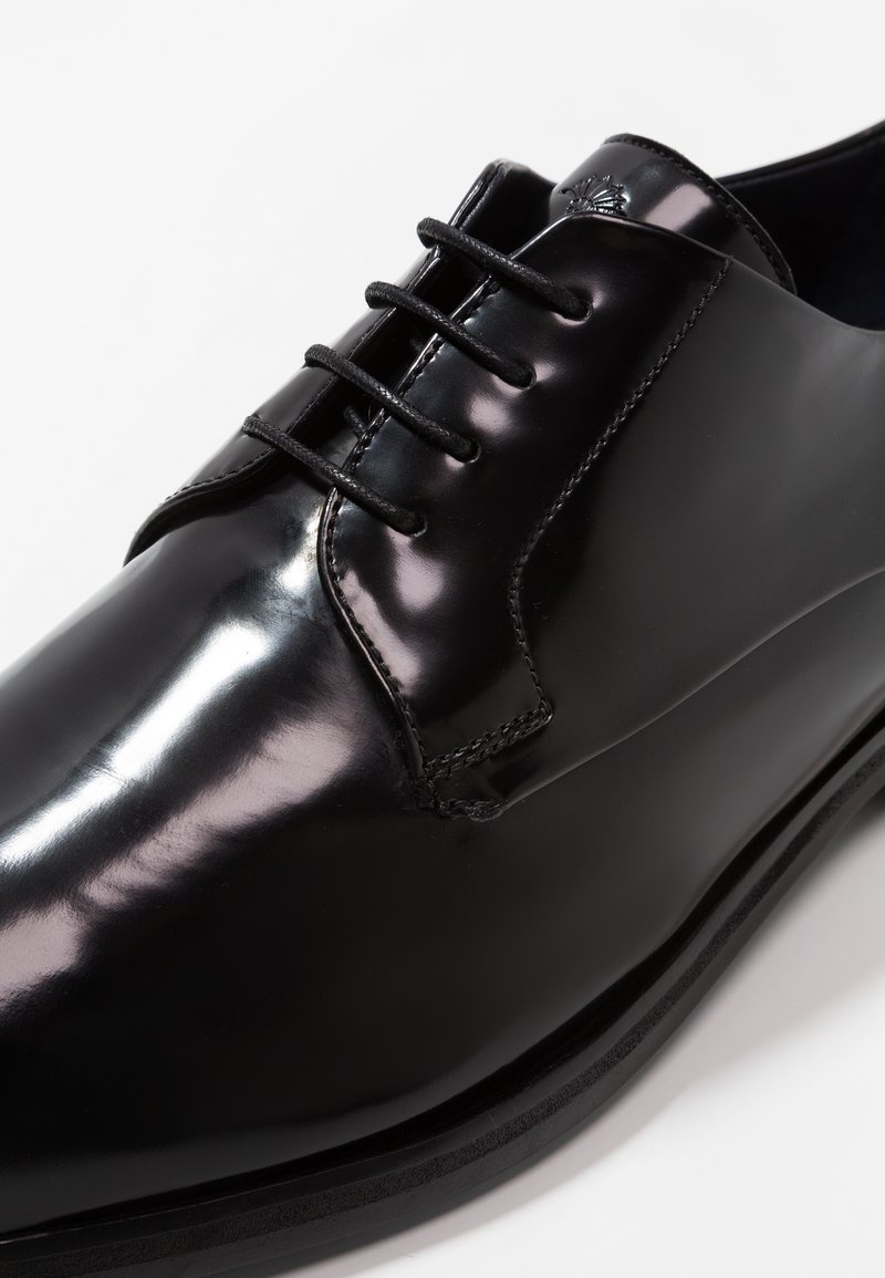 Schwarze Lederdressschuhe mit glänzender Oberfläche, ausgestattet mit sechs Ösen, schwarzen Schnürsenkeln und dezenten Steppnähten entlang des Kragens und der Sohle.