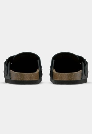 Paire de sandales slides noires avec semelles en liège et sangles latérales réglables, vues de dos sur fond blanc.