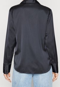 Zwarte satijnen blouse met lange mouwen en een kraaghalslijn, gladde textuur en knoopmanchetten, gecombineerd met lichtblauwe jeans.