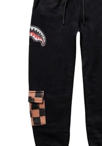 Pantaloni della tuta neri con una grafica di mascella di squalo sulla coscia e una tasca a scacchi arancione e nera. Presentano un girovita con cordino e una vestibilità rilassata.