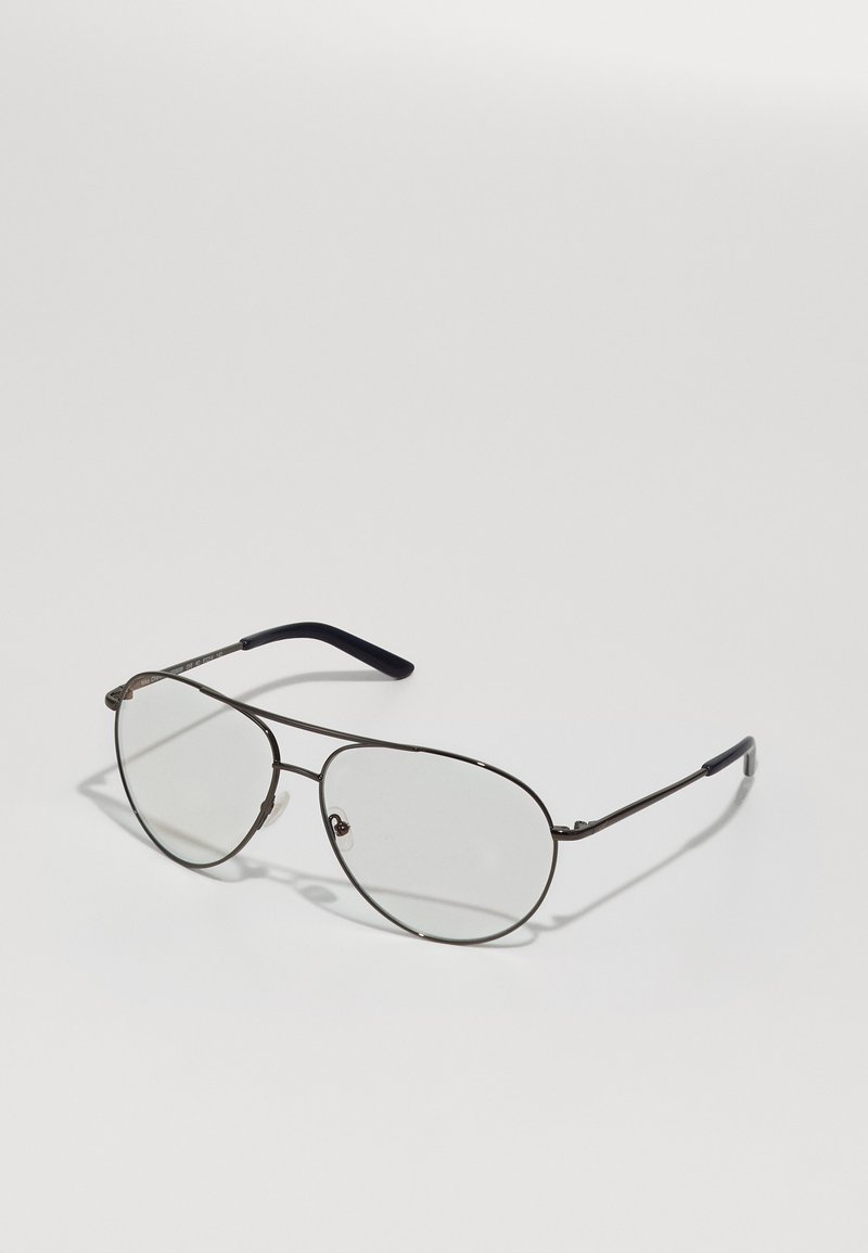 Óculos de armação metálica com grandes lentes ovais. A armação é de metal escuro com um design fino e pontas de haste em preto. As lentes são transparentes.