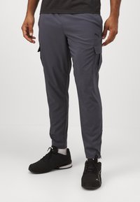 Grå cargo-bukser med slim fit, laget av lett materiale, med sidelommer og logo på låret. Kombinert med svarte joggesko.