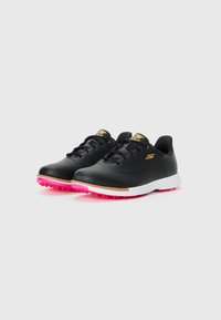 Black golf shoes with pink rubber spikes, white midsole, and gold accents. Feature a smooth leather-like upper and lace-up design.
