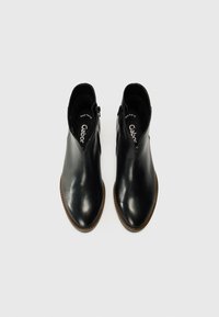 Bottes noires en cuir à la cheville avec une finition lisse, bout arrondi et fermeture éclair sur le côté. Semelle brun robuste avec des détails subtils le long du bord.
