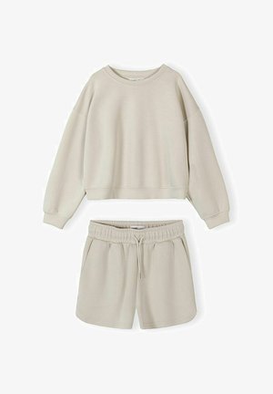 Set lounge bej din două piese, cu bluză cu mâneci lungi și guler rotund, și șorturi cu talie elastică și șnur, pe fundal alb.