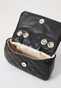 Sac en cuir noir matelassé avec un fermoir à pression métallique et des éléments en or. L'intérieur est en tissu beige sans motifs ni poches visibles.