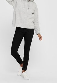 Hoodie grigio corto con cordino, jeans neri slim-fit e sneaker bianche. Superfici lisce; design casual e funzionale.