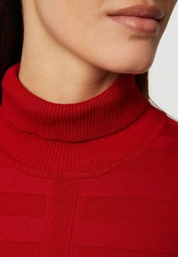 Pull côtelé rouge avec une texture en relief et des rayures horizontales distinctes sur le corps, gros plan du col et des détails du tissu.