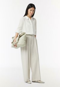 Weißes, strukturiertes Hemd mit Knöpfen; hellgraue, weit geschnittene Hose; weiche grüne Handtasche mit gerafften Akzenten; beigefarbene spitze Ballerinas.
