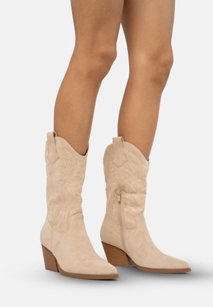 Beige suede cowboylaarzen met een spitse neus, decoratieve stiksels, een zijrits en een gestapelde hak. Getextureerd oppervlak met bloemmotieven.