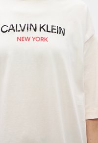 Λευκό βαμβακερό μπλουζάκι με τη φράση "CALVIN KLEIN" σε μαύρο χρώμα και "NEW YORK" σε κόκκινο κέντημα στο στήθος. Κοντά μανίκια, άνετη εφαρμογή.