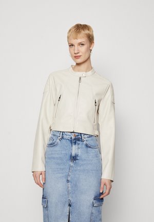 White leather cropped jacket with a high collar, front zip closure, and two zippered pockets. Worn over a denim skirt.