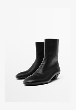 Black leather ankle boots with a pointed toe and a sleek, high shaft. Features a zipper closure and a small, tapered heel. Smooth texture.