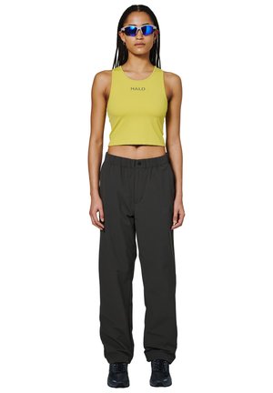 Żółty, krótki top z logo "HALO", w połączeniu z luźnymi ciemnoszarymi spodniami i czarnym obuwiem. Model nosi niebieskie okulary przeciwsłoneczne.
