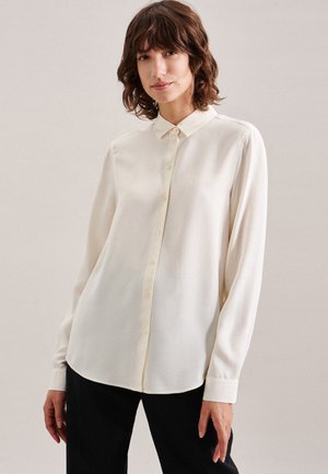 Blouse à manches longues de couleur crème, en tissu lisse, avec un devant à boutons et un col classique, dotée d'une coupe décontractée et de manches à poignets.