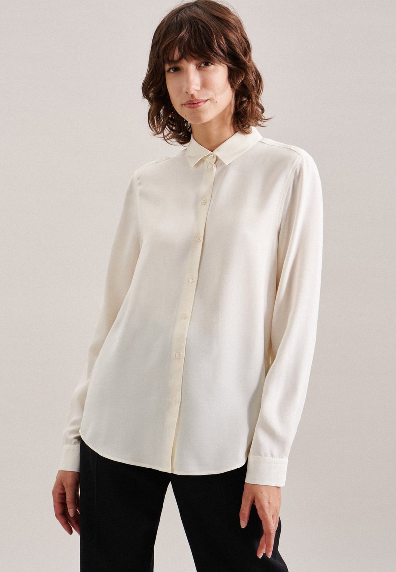 Cremfarbene Bluse mit langen Ärmeln aus glattem Stoff, ausgestattet mit einer Knopfleiste und einem klassischen Kragen, in entspannter Passform und mit geknöpften Ärmeln.