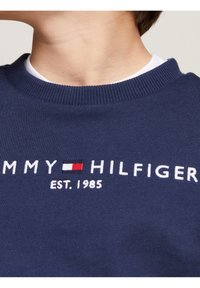 Granatowy bawełniany sweatshirt z okrągłym dekoltem, ribbowanym kołnierzem i haftowanym logo w czerwono-biało-niebieskich akcentach.