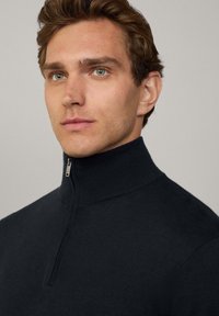 Svart zip-tröja med hög krage i mjukt, stickat material och en stilren dragkedjedetalj vid halsen.