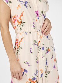 Robe florale en pêche pastel, avec des manches courtes, une taille cintrée avec un lien et des motifs floraux colorés en violet, orange et vert.