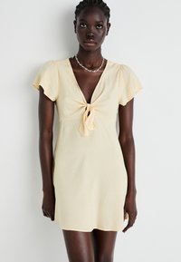 Yellow short dress with cap sleeves, a V-neckline, and a front tie. Made from lightweight fabric, features a smooth texture.