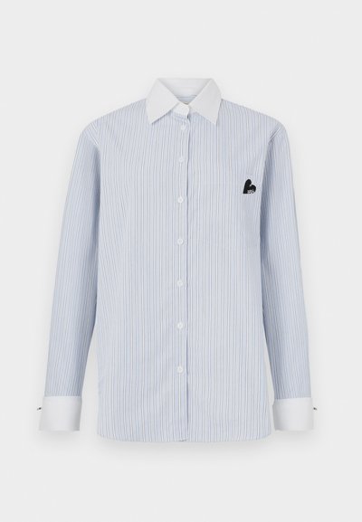 Striped long-sleeve shirt in light blue with white stripes. Features a white collar, front buttons, and a pocket with a black logo detail.