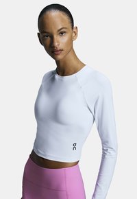 Langärmliges weißes Sportoberteil mit tailliertem Schnitt und schwarzen Logo-Details am Saum, kombiniert mit hochtaillierten pinken Leggings.