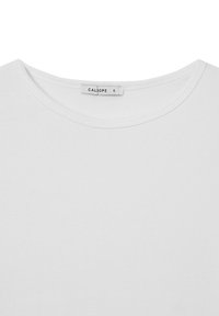 T-shirt bianco in cotone con una texture a coste e scollatura rotonda. Etichetta con il marchio "CALIOPE" e taglia "S" visibile al colletto.