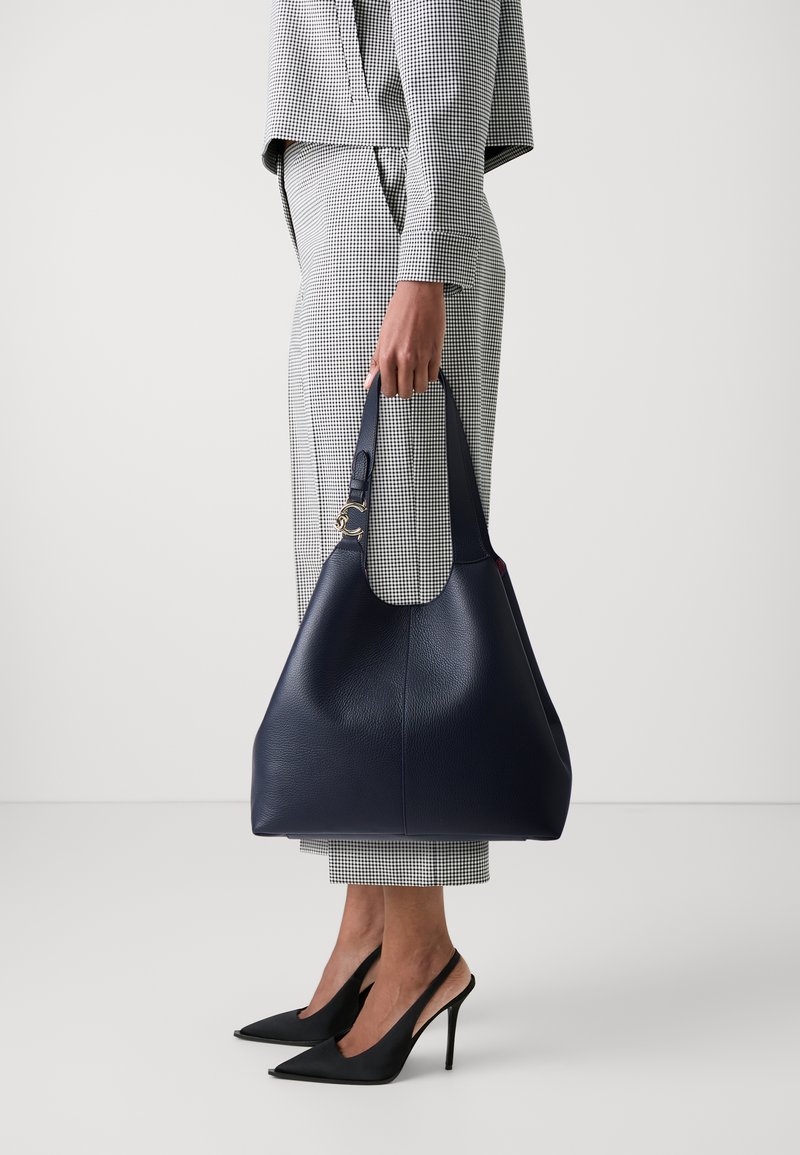 Navy leather handbag with a wide, rounded shape and textured finish. Features a single handle and gold hardware detail.