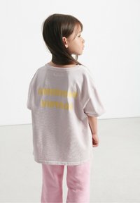 Šviesiai rožinė per didelė marškinė su „AMERICAN VINTAGE“ drąsiu geltonu užrašu nugaroje, derinama su švelniais rožiniais kelnais. Lygus paviršius.