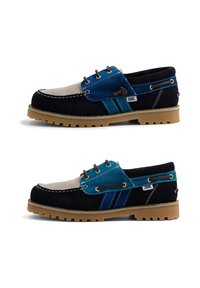 Deux chaussures bateau en daim bleu, noir et beige avec des lacets marron et des semelles en caoutchouc, vues de côté sur fond blanc.