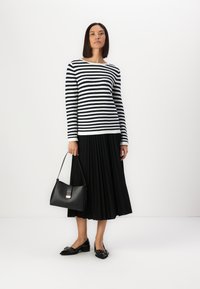 Schwarz-weiß gestreiftes Langarmshirt, plissierter schwarzer Rock, schwarze Handtasche und schwarze Ballerinas mit Verzierungen.