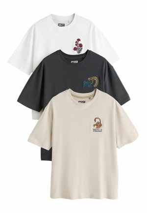 Tre t-shirts med korte ærmer og rund hals i hvid, sort og beige, hver med en lille grafik på brystet og et mærke med brandnavn inde i kraven.