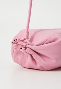 Rosa skinnveske med en rynket design, glatt tekstur og en slank skulderrem. Har subtile sømmer og en myk, avrundet form.