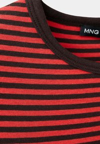 Gros plan d’un tissu rayé horizontalement rouge et noir avec un col côtelé noir et une étiquette MNG visible.