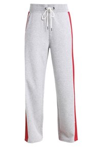 Grå sweatshirtbyxor i mjukt tyg, med dragsko i midjan, sidofickor och röda sidostråk. Rakt bendesign med minimal textur.