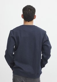 Felpa blu navy realizzata in morbido tessuto, con collo a giro e maniche lunghe con polsini a coste. Nessun motivo o hardware visibile.