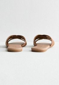Bruna platta sandaler med två böjda remmar, en slät imitation läderfinish och en minimalistisk design. Öppen tå med platt sula.