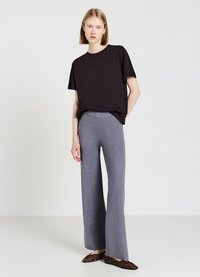 Schwarzes kurzärmliges T-Shirt, graue weit geschnittene Hose, strukturierter Stoff, kombiniert mit Ballerinas im Leopardenmuster, minimalistischer Hintergrund.