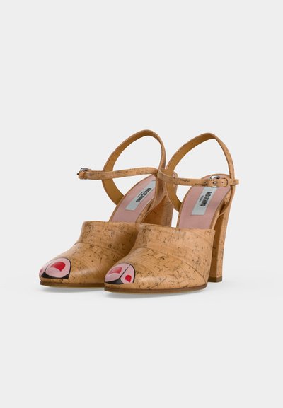 Ζεύγος σανδαλιών με τακούνι και υφή φελλού, με λουράκια στον αστράγαλο και ζωγραφισμένα κόκκινα σχέδια στα νύχια των δακτύλων.