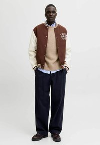 Brown and cream varsity jacket with a front logo, beige knit sweater, navy wide-leg trousers, and dark shoes. Simple color palette and textures.