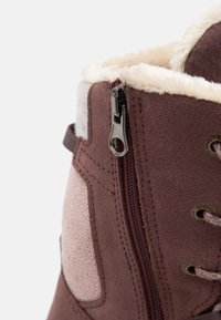 Braune Wildlederstiefel mit einem cremefarbenen Kunstfellkragen, seitlichem Reißverschluss und strukturiertem Stoffpanel. Verfügt über braune Schnürsenkel und metallische Ösen.