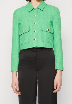 Groene gestructureerde cropped jas met gouden knopen en klepzakken, gedragen met zwarte broek met hoge taille.