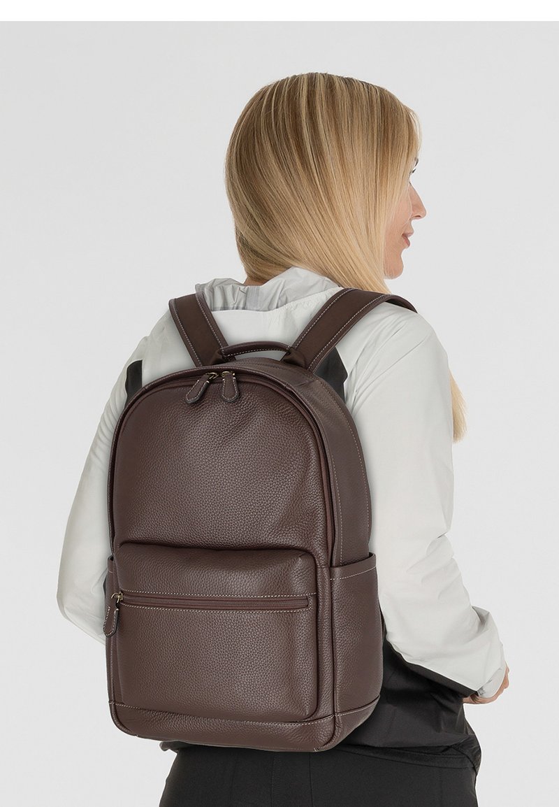 Sac à dos en cuir brun avec une surface texturée, doté de bretelles réglables, d'une poche zippée à l'avant et d'un design arrondi.