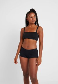 Schwarzes Baumwoll-Crop-Top und passende Shorts im Boxerschnitt. Das Top hat dünne Träger und einen quadratischen Ausschnitt; die Shorts sind eng anliegend.