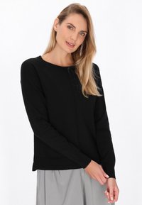 Pulover lung negru, cu mâneci lungi, guler rotund și manșete cu elastic. Are un design simplu, cu o textură netedă. Poartă-l peste o fustă gri.